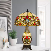 A multicolor 16 inch Tiffany style cluster table lamp with a stained glass shade and a metal base, displaying a geometric pattern, placed on a white surface in a room.