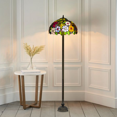 A Tiffany floor lamp with a handcrafted stained glass shade featuring a floral pattern, placed on a metal base, in a room corner.