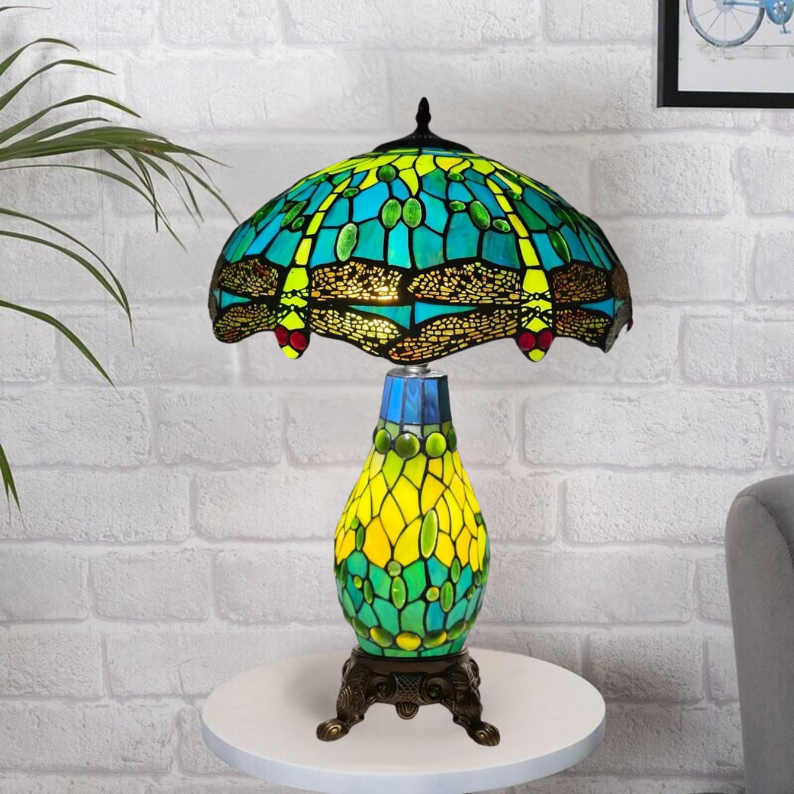 A colorful Tiffany style clustered table lamp with a stained glass shade and a metal base, placed on a white surface against a brick wall background.