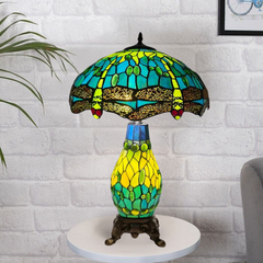 A colorful Tiffany style clustered table lamp with a stained glass shade and a metal base, placed on a white surface against a brick wall background.