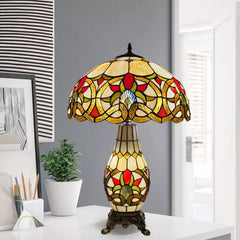 A multicolor 16 inch Tiffany style cluster table lamp with a stained glass shade and a metal base, displaying a geometric pattern, placed on a white surface in a room.