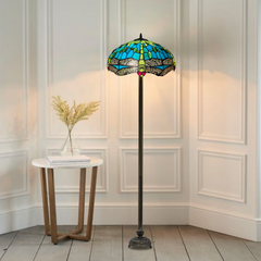 A beautiful grreen color stained glass large tiffany floor lamp placed in a white background room baside a table