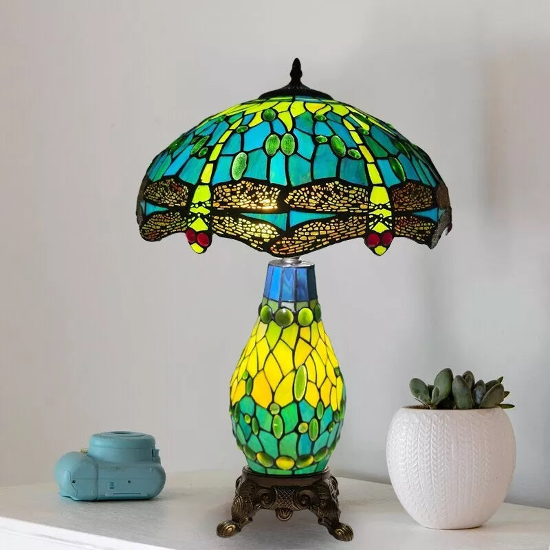 A green stained glass 16 inch tiffany cluster table lamp placed on a white table with a potted plant