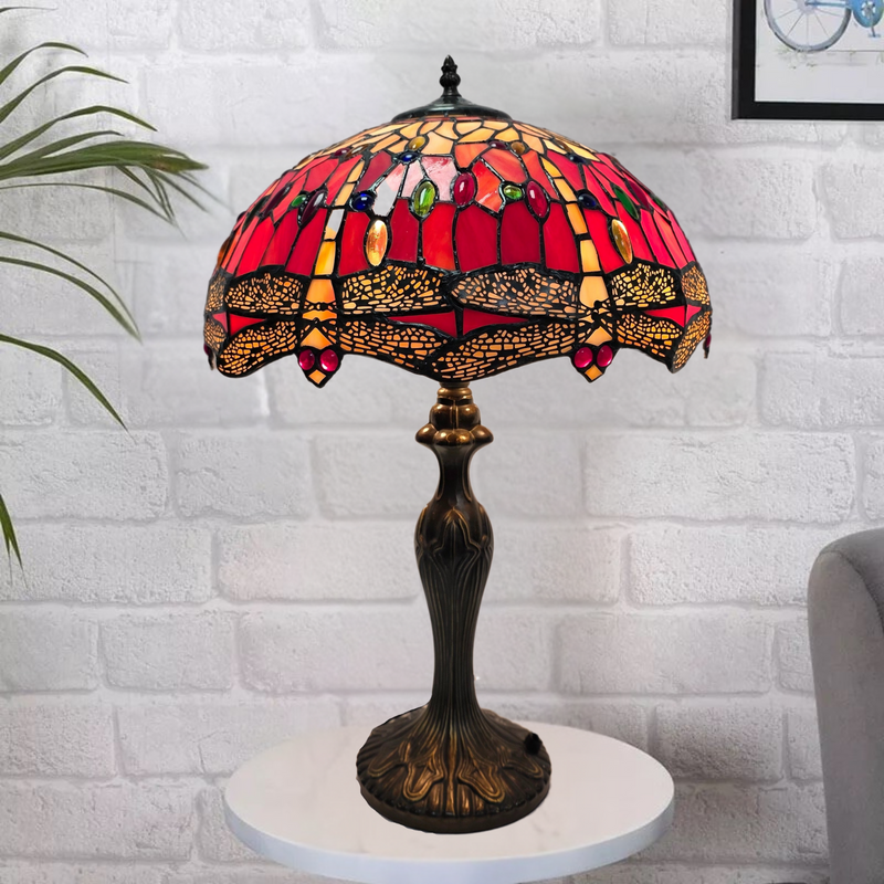 Red Tiffany table lamp with stained glass shade on a white platform against a white brick wall.
