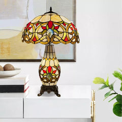A multicolor stained glass vintage tiffany style cluster table lamp placed on a white table and a painting at its back